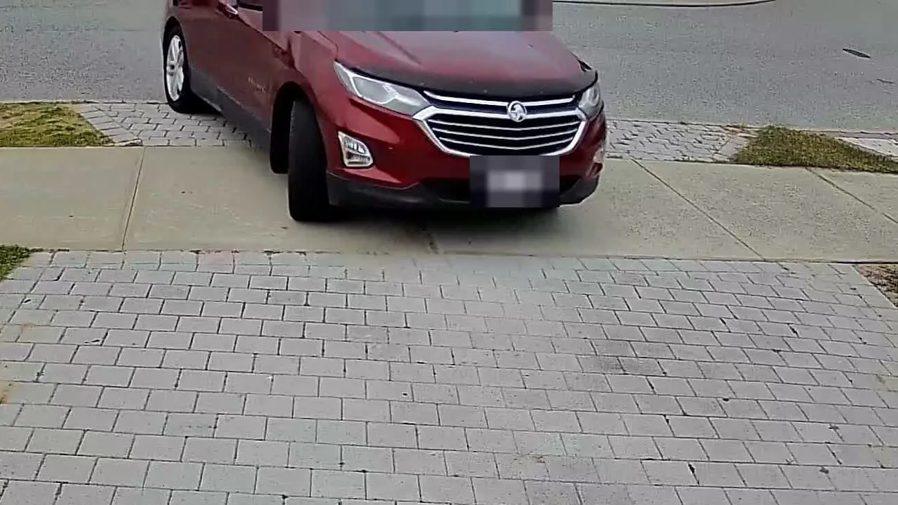 A red SUV turning into a paved driveway, seen from above the garage. The number plate is blurred.